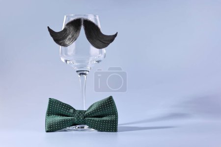 Téléchargez les photos : Visage d'homme fait de moustache artificielle, noeud papillon et verre à vin sur fond bleu clair. Espace pour le texte - en image libre de droit