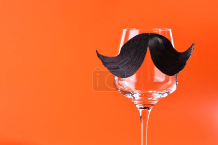 Téléchargez les photos : Visage d'homme fait de moustache artificielle et verre de vin sur fond orange. Espace pour le texte - en image libre de droit