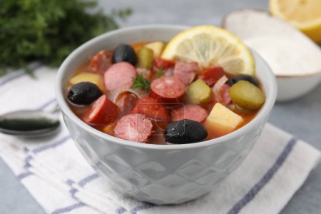 Téléchargez les photos : Soupe de viande solyanka avec de fines saucisses fumées sèches dans un bol sur une table grise, gros plan - en image libre de droit