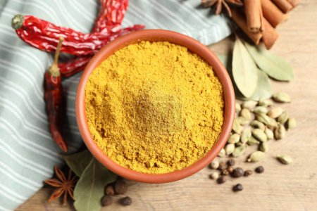 Curry powder in bowl and other spices on wooden table, flat lay