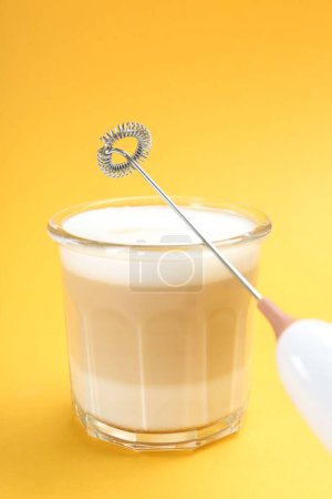 Mini mezclador (espuma de leche) y sabroso capuchino en vidrio sobre fondo amarillo