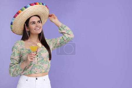 Mujer joven en sombrero mexicano con cóctel sobre fondo violeta. Espacio para texto