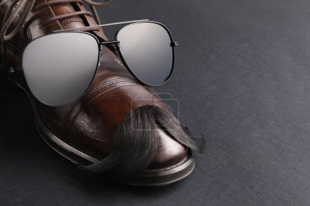 Téléchargez les photos : Moustache artificielle, chaussures et lunettes de soleil sur fond noir, gros plan. Espace pour le texte - en image libre de droit