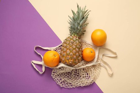 Téléchargez les photos : Sac à ficelle avec ananas frais et oranges sur fond de couleur, plat - en image libre de droit