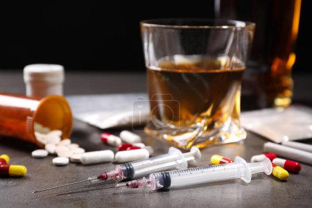 Téléchargez les photos : Alcool et toxicomanie. Seringues, whisky en verre, pilules et cocaïne sur table grise, gros plan - en image libre de droit