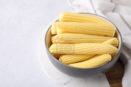 Tasty fresh yellow baby corns in bowl on white table, space for text