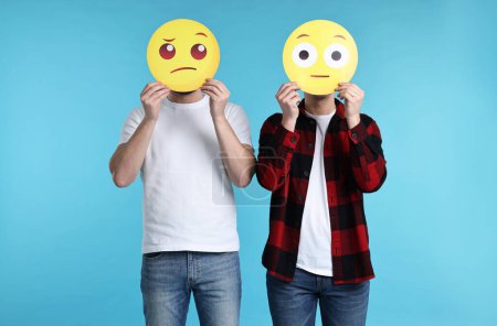 Foto de Gente cubriendo caras con emoticonos sobre fondo azul claro - Imagen libre de derechos