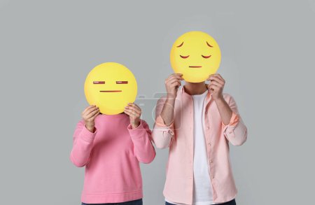 Foto de Gente cubriendo caras con emoticonos tristes sobre fondo gris - Imagen libre de derechos