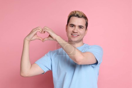 Téléchargez les photos : Jeune homme montrant geste de coeur avec les mains sur fond rose - en image libre de droit