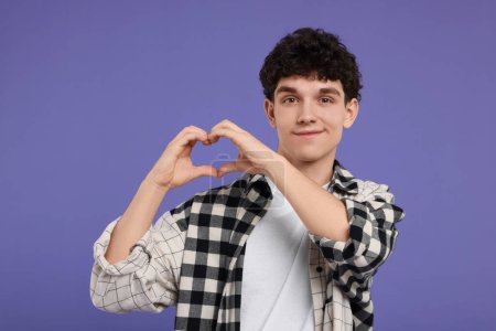 Téléchargez les photos : Jeune homme heureux montrant geste de coeur avec les mains sur fond violet - en image libre de droit