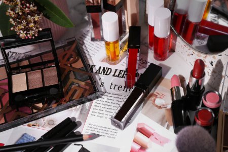 Foto de Brillante brillo labial entre diferentes productos cosméticos y revista de moda en la mesa - Imagen libre de derechos