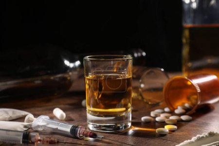 Téléchargez les photos : Alcool et toxicomanie. Whisky en verre, seringues, pilules et cocaïne sur table en bois - en image libre de droit