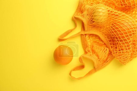 Téléchargez les photos : Sac à ficelle avec des oranges fraîches sur fond jaune, vue de dessus. Espace pour le texte - en image libre de droit