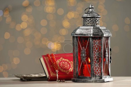 Arabic lantern, Quran and misbaha on table against blurred lights
