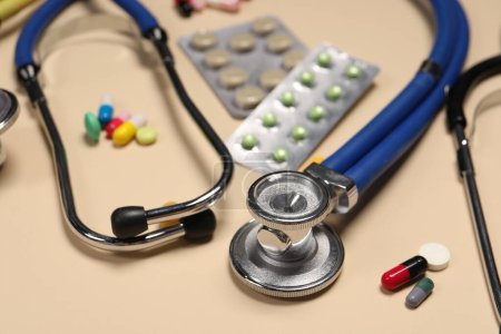 Photo for Stethoscope and pills on beige background, closeup. Medical tool - Royalty Free Image