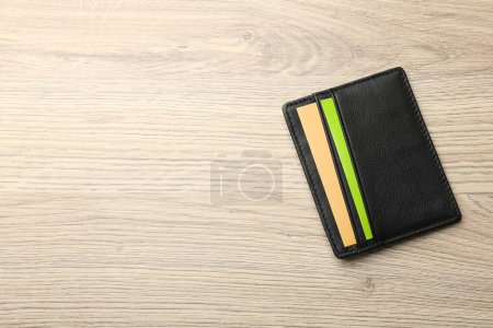 Leather business card holder with colorful cards on wooden table, top view. Space for text