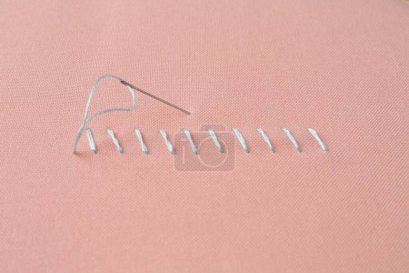 Sewing needle with thread and stitches on coral cloth, closeup