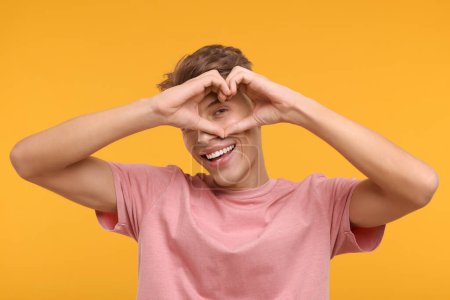 Glücklicher Mann zeigt Herz-Geste mit Händen auf orangefarbenem Hintergrund