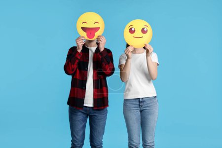 Foto de Gente cubriendo caras con emoticonos sobre fondo azul claro - Imagen libre de derechos