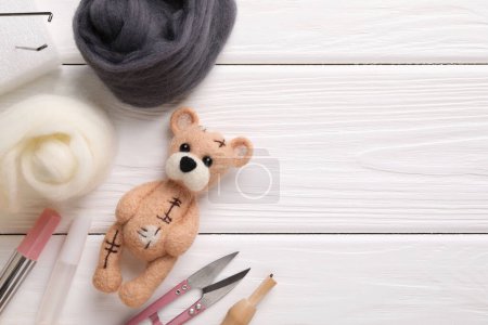 Felted bear, wool and tools on white wooden table, flat lay. Space for text