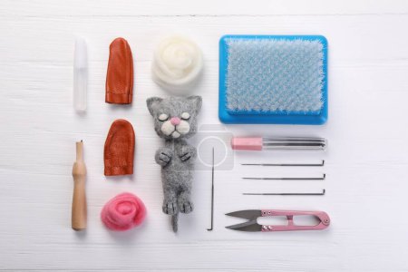 Gefilzte Katze, Wolle und verschiedene Werkzeuge auf weißem Holztisch, flach gelegt