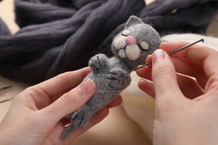 Woman felting cute toy cat from wool at table, closeup