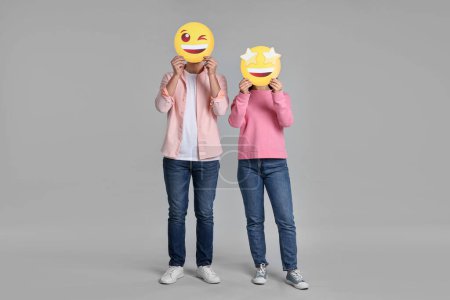 Foto de Gente cubriendo caras con emoticonos felices sobre fondo gris - Imagen libre de derechos
