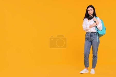 Student with backpack and headphones on yellow background. Space for text