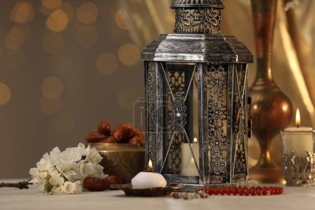 Arabic lantern, misbaha, candles, dates and flowers on table against blurred lights