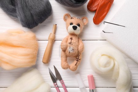 Felted bear, wool and tools on white wooden table, flat lay
