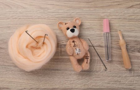 Felted bear, wool and tools on wooden table, flat lay
