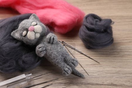 Felted cat, wool and tools on wooden table, closeup