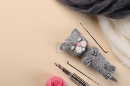Felted cat, wool and tools on beige table, flat lay. Space for text