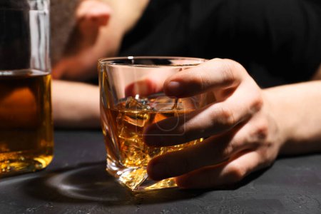 Téléchargez les photos : L'alcoolisme. Homme avec verre de whisky à la table sombre texturée, mise au point sélective - en image libre de droit