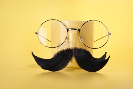Téléchargez les photos : Visage d'homme fait de moustache artificielle, verres et tasse sur fond jaune - en image libre de droit