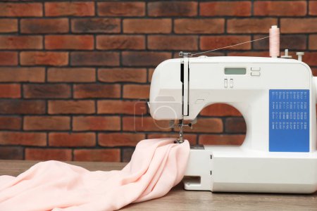 Photo for Sewing machine with fabric on wooden table against brick wall - Royalty Free Image