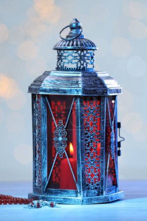 Arabic lantern and misbaha on table against blurred lights