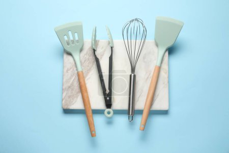 Téléchargez les photos : Différentes spatules, fouet et pinces sur fond bleu clair, pose plate - en image libre de droit