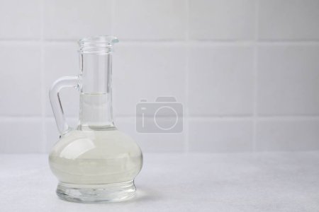 Vinegar in glass jug on light table, space for text
