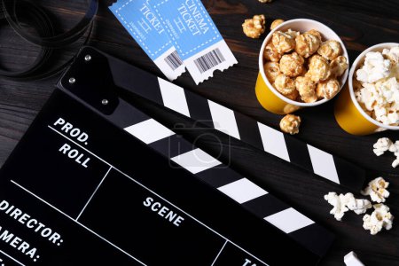 Klappbrett, Kinokarten, Popcorn und Filmrolle auf Holztisch, flach gelegt
