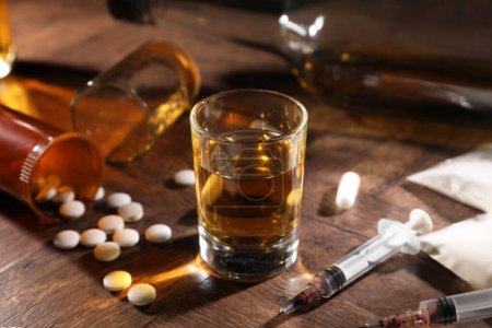 Téléchargez les photos : Alcool et toxicomanie. Whisky en verre, seringues, pilules et cocaïne sur table en bois - en image libre de droit