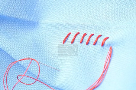 Téléchargez les photos : Aiguille à coudre avec fil et points de suture sur tissu bleu clair, gros plan - en image libre de droit
