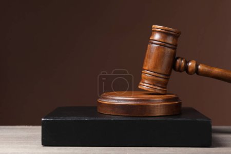 Law. Book and gavel on wooden table against brown background, space for text