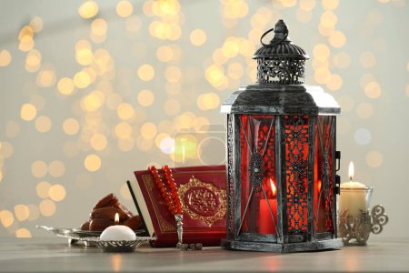 Arabic lantern, Quran, misbaha, candles and dates on table against blurred lights