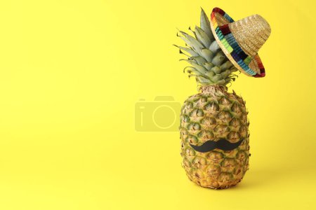 Téléchargez les photos : Ananas avec chapeau de sombrero mexicain et fausse moustache sur fond jaune, espace pour le texte - en image libre de droit