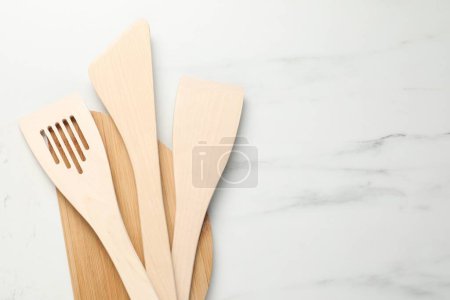 Board with different wooden spatulas on light marble table, top view. Space for text