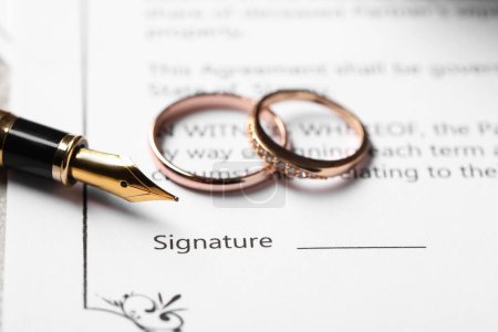 Contrato de matrimonio, pluma estilográfica y anillos de boda en la mesa, primer plano