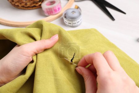 Woman with sewing needle and thread embroidering on cloth at white wooden table, closeup