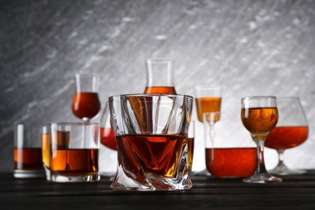 Different delicious liqueurs in glasses on dark wooden table