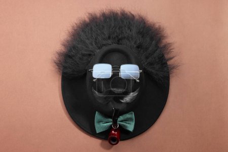 Téléchargez les photos : Visage d'homme fait de moustache artificielle, lunettes de soleil et chapeau sur fond brun, vue de dessus - en image libre de droit
